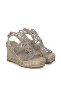 Sandali con zeppa beige, caratterizzati da cinturini decorativi con ritagli e dettagli metallici. Presentano una suola rivestita in juta e una chiusura con fibbia alla caviglia.