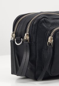 Sort lædertaske med to lynlåskompartments, sølvlynlåse og en side-ring til fastgørelse; struktureret ydre med glatte accenter.