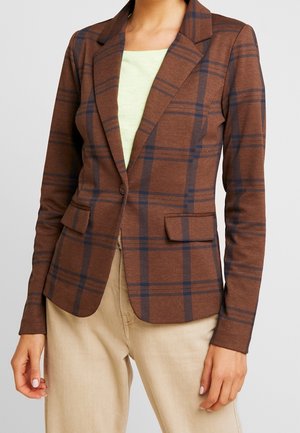 Bruine geruite blazer met enkele knoop en inkeping revers, gedragen over een lichtgroene top en beige broek, afgebeeld van nek tot heup.