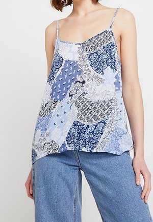 Débardeur patchwork en bleu clair avec divers motifs bleus, fines bretelles et coupe ample. Tissu léger avec une texture douce.