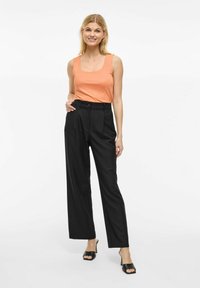 Top portocalie fără mâneci cu decolteu pătrat și pantaloni negri cu talie înaltă și picioare largi. Material neted și croiala ajustată. Pantofi negri cu vârful descoperit.
