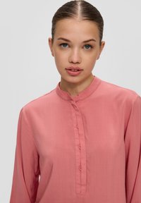 Lichtroze blouse met lange mouwen, een mandarinnekraag en een knoopsluiting. Soepele textuur en een iets losse pasvorm, geschikt voor casual kleding.