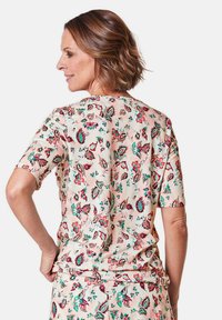 Short-sleeved shirt in light pink fabric featuring a colorful floral pattern. The back view shows a loose fit and round neckline.