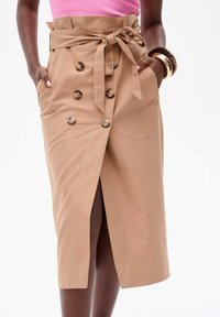 Jupe-emballage kaki avec taille haute, poches latérales, lien à la taille, détail de boutons double boutonnage et fente frontale pour faciliter les mouvements.