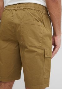 Khaki cargo shorts with an elastic waistband, back pocket, and side pocket. Made from soft, textured cotton fabric.