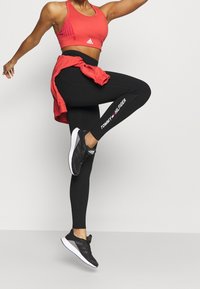 Czerwony sportowy krótki top z prążkowanymi akcentami, czarne legginsy z logo "TOMMY HILFIGER" oraz czarne buty sportowe z białą podeszwą.