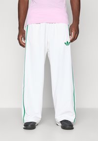 Vita avslappnade sweatpants med gröna sidostråk och en grön logotyp på vänster lår, tillverkade av ett mjukt, lättviktigt tyg.