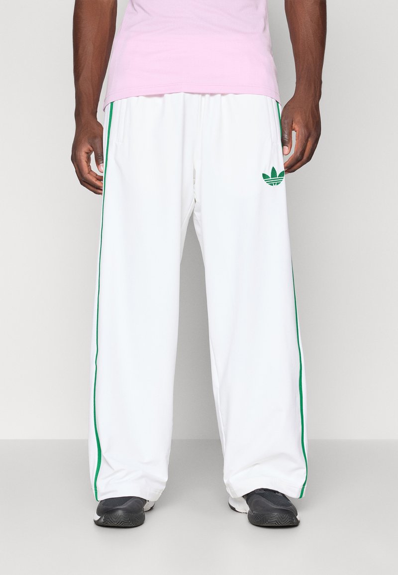 Vita avslappnade sweatpants med gröna sidostråk och en grön logotyp på vänster lår, tillverkade av ett mjukt, lättviktigt tyg.
