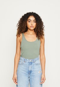 Olive green tank top made of soft fabric with a scoop neckline, paired with high-waisted light blue distressed jeans.