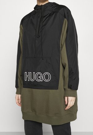 Felpa con cappuccio con parte superiore in nylon nero e parte inferiore in cotone verde oliva. Presenta una tasca frontale e il logo "HUGO" in lettere bianche.