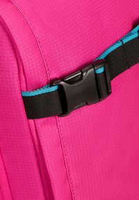 Bolsa de tela rosa con superficie texturizada; presenta una hebilla de plástico negra con acentos turquesa y una correa lateral compacta.