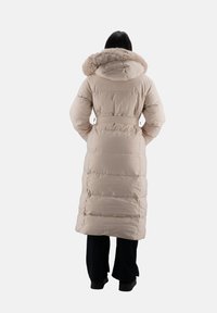 Lungo cappotto beige imbottito con cappuccio bordato di pelliccia, vita con cintura, texture trapuntata e lunghezza fino al polpaccio. La vista da dietro mette in evidenza le cuciture orizzontali.