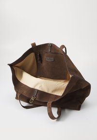 Hnědá semišová taška přes rameno s bavlněným vnitřkem, otevřeným vrchem, dvěma uchy a zipovou kapsou uvnitř. Minimalistický design a pevný materiál.