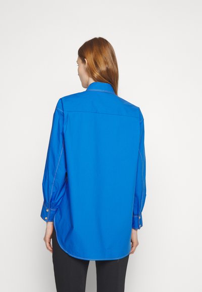 Μπλε βαμβακερό πουκάμισο με μακριά μανίκια, κουμπωτές μανσέτες και αντίθετη λευκή ραφή. Διαθέτει κλασικό γιακά και καμπύλη στρίφωμα.