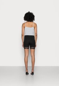 Camisola grigia con spalline sottili, abbinata a pantaloni corti neri con bordo in pizzo. La modella indossa scarpe con tacco alto nere.