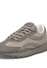 Sneaker grigio in suede con design a strati, pannelli testurizzati, lacci piatti e suola in gomma rialzata. Presenta un branding minimale sulla linguetta.