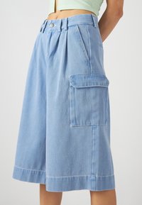 Light blue cargo shorts made of denim with a loose fit, pleats, a front button closure, and side pockets.