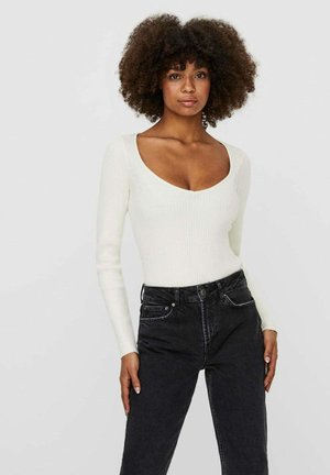Top a maniche lunghe a costine in bianco sporco con scollatura profonda, abbinato a jeans neri in denim a vita alta con tasche frontali.