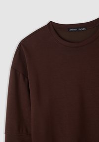 T-shirt marrone a maniche corte con scollatura rotonda, realizzato in tessuto morbido; presenta una sottile trama e dettagli di cucitura sulle maniche.