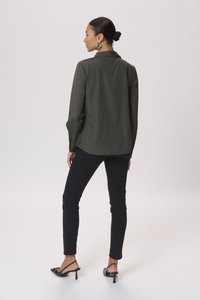 Blusa verde scuro con maniche lunghe e colletto, abbinata a pantaloni neri a vestibilità slim e sandali neri con tacco. Tessuto morbido con un taglio classico.