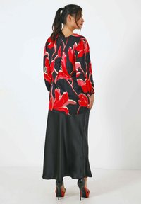 Satijnen zwarte rok met een levendig rood bloemenpatronen top, voorzien van lange mouwen en een ronde hals. Hoge rode hakken maken de look compleet.