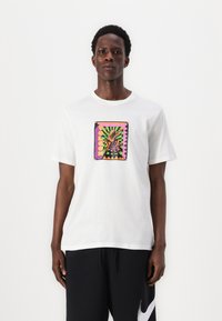 White cotton t-shirt with crew neck and short sleeves. Front features colorful graphic with geometric patterns and a frog design.