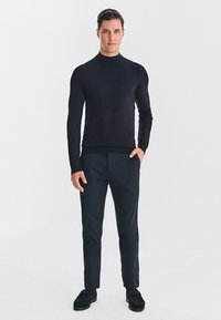 Czarny sweter z golfem wykonany z gładkiej tkaniny, zestawiony z ciemnymi spodniami. Dopasowany krój z prążkowanymi mankietami i teksturowaną powierzchnią. Minimalistyczny design.