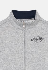 Grijze zip-up jack van textiel, met een zwart "CHAMPION" logo op de linkerkant van de borst en een marineblauwe kraag.