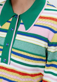 Gebreide polo met groene kraag, meerkleurige horizontale strepen in geel, roze, blauw en rood, met blauwe knoopaccenten.