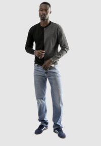 Camicia a maniche lunghe color block in nero e grigio abbinata a jeans blu chiaro e sneakers scure, con scollatura a girocollo e design aderente.