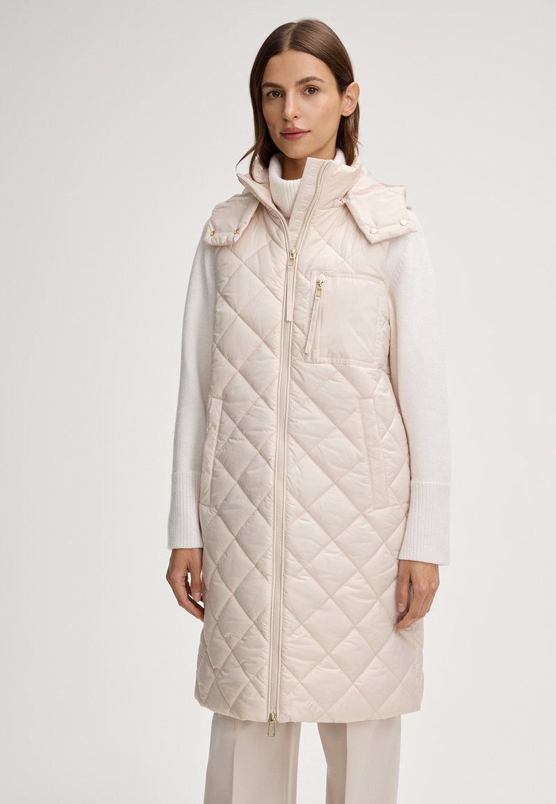 Gilet trapuntato crema con collo alto, zip frontale e tasche laterali. Presenta bottoni a pressione sulle spalle e una tasca decorativa con zip.