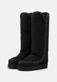 Botas altas de ante negro hasta la rodilla con punta redonda, forro de borrego y costuras decorativas a lo largo de los bordes. Suela de goma plana.