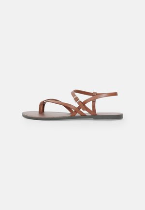 Sandales plates en cuir marron avec des lanières croisées, un design à bout ouvert et une sangle à boucle autour de la cheville. Texture lisse et style minimaliste.