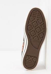 Semelle de sneaker Converse All Star, en caoutchouc marron avec un motif géométrique texturé. Présente un bord écru et un marquage en relief près du talon.