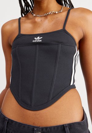 Sort ribbet cropped tank top med smalle stropper, med et hvidt Adidas-logo og kontrasterende hvide sidestropper. Skræddersyet pasform, tekstureret stof.