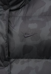 Čierna maskáčová zateplená bunda s uzavretým zipsom, textúrovanou tkaninou a malým vyšitým logom Nike na hrudi.