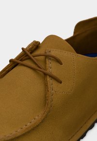 Κοντινή λήψη ταμπά δερμάτινου παπουτσιού από σουέντ με καφέ δερμάτινα κορδόνια δεμένα σε απλό φιόγκο και λεπτομερείς ραφές κατά μήκος των άκρων.