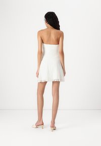 Robe blanche sans bretelles avec un design en dentelle texturée, corsage ajusté et jupe évasée, présentant un délicat bord en dentelle à l'ourlet.