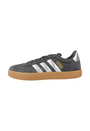 Baskets Adidas en daim gris avec des bandes argentées, une semelle en gomme, des lacets noirs et un logo Adidas doré sur le côté, vues de l'extérieur.