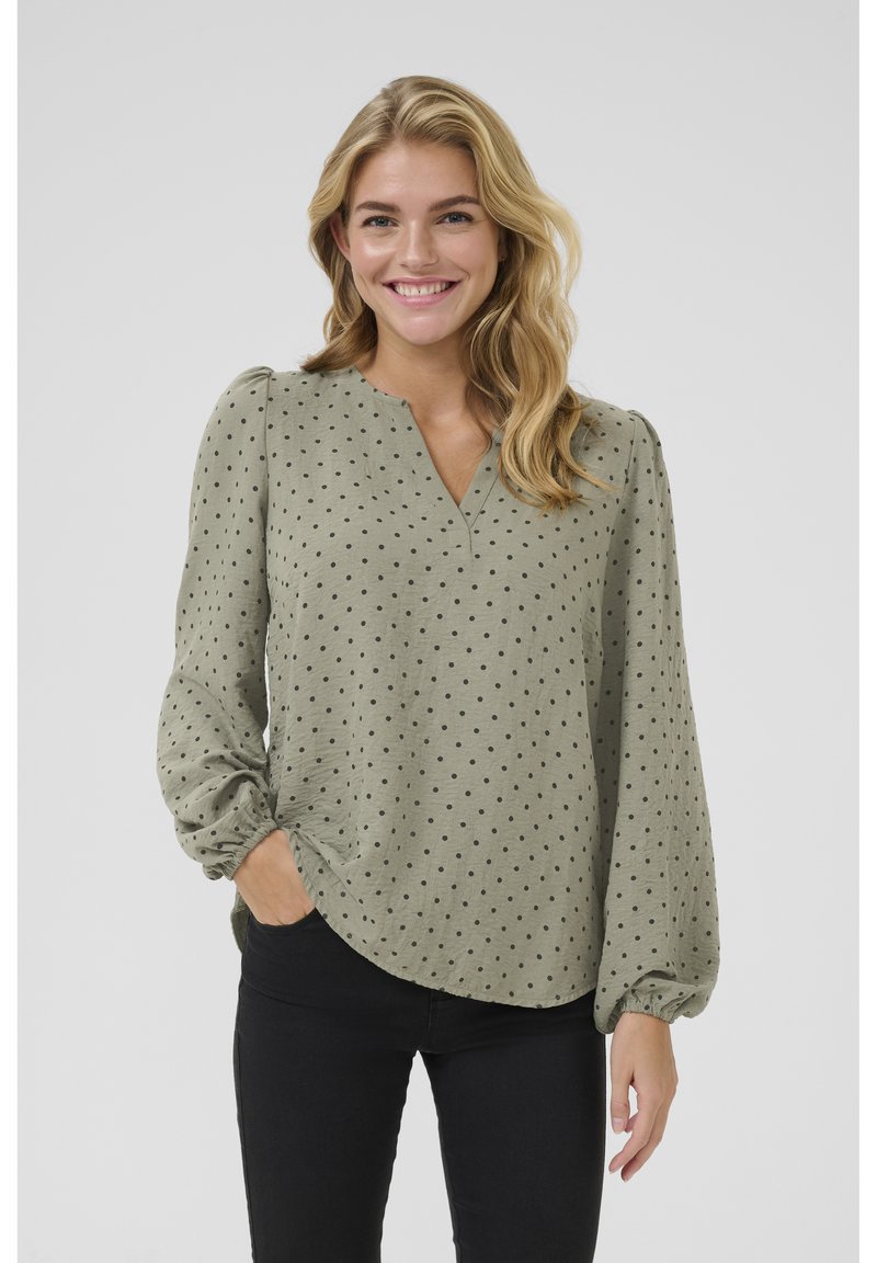 Lange mouw, olijfgroene blouse met een V-hals en zwarte stippen. De stof heeft een zachte textuur met gathered manchetten en een gebogen zoom.
