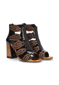 Botines de tobillo de charol negro con punta abierta, que presentan tachuelas decorativas en oro y púrpura. Tacón grueso, diseño recortado y acentos texturizados.