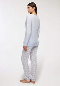 Top azzurro chiaro a maniche lunghe con scollo rotondo e tessuto morbido, abbinato a pantaloni azzurri chiari con motivi a nuvola bianchi.