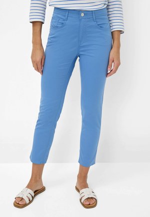 Pantaloni elasticizzati blu dal fit slim, con due tasche frontali e lunghezza alla caviglia, abbinati a sandali bianchi a infradito e una maglietta a righe.