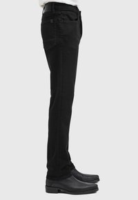Vaqueros de mezclilla negros con corte ajustado, que cuentan con cinco bolsillos y una textura suave. Combinados con unos zapatos de vestir de cuero negros.