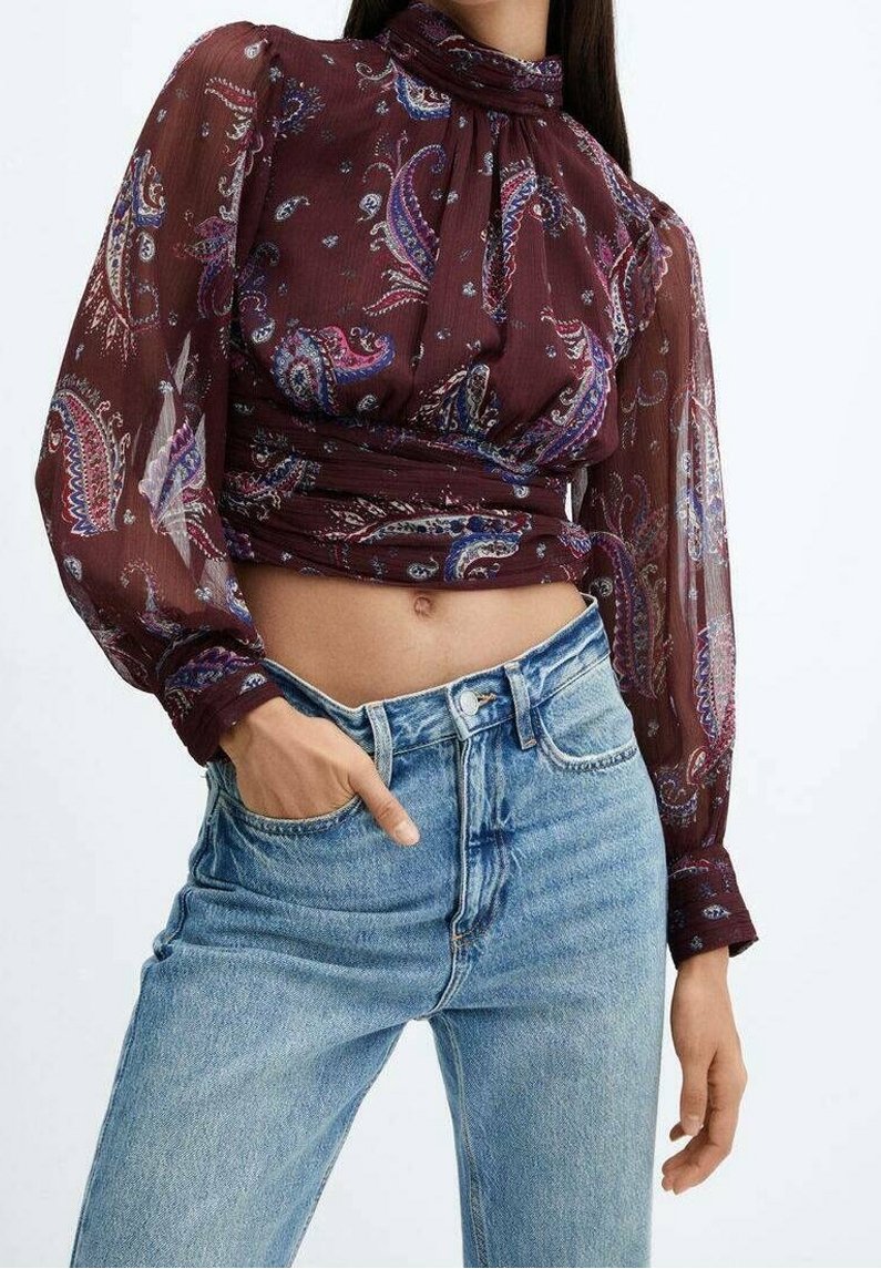 Blouse maroon à motif paisley avec des manches longues transparentes, col haut et taille froncée, associée à un jean taille haute bleu clair.