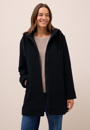 Manteau en polaire noire avec fermeture éclair sur le devant et capuche, présentant une surface texturée, des poches latérales et une coupe droite épurée.