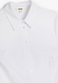 Camicia bianca con colletto classico; realizzata in tessuto liscio con dettagli di bottoni sul davanti e una texture liscia.