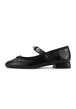 Chaussure Mary Jane en cuir noir avec petit talon, bride ajustable avec clous dorés et petit nœud décoratif à l’avant.