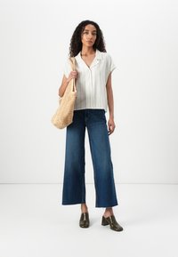 White striped short-sleeve button-up shirt, blue wide-leg jeans, gold heeled mules, and a woven beige handbag. Minimalist design.
