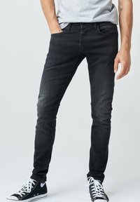 Jeans negros ajustados hechos de tela de mezclilla, con cinco bolsillos, cintura clásica y un sutil desgastado. Combinados con zapatillas negras.